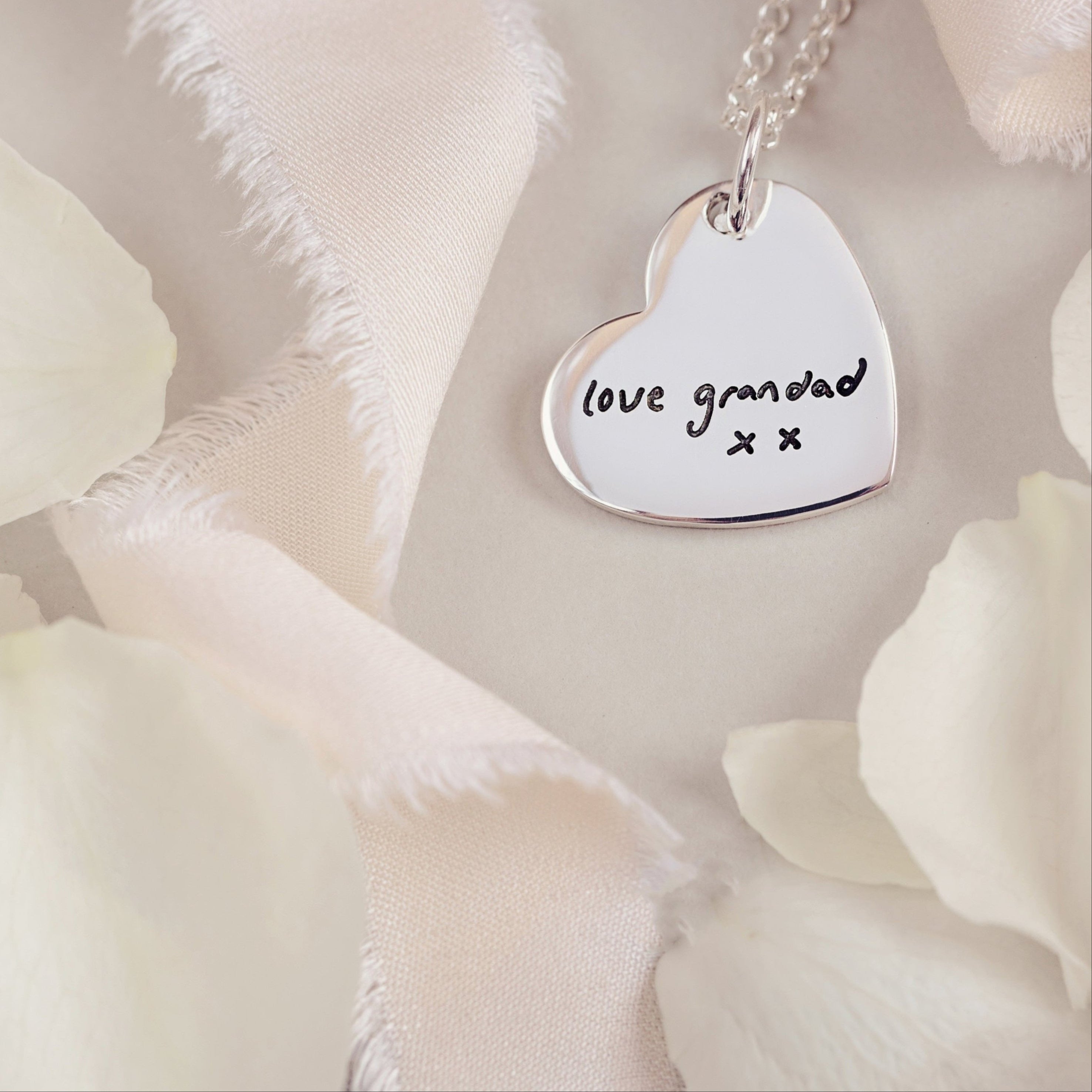 A silver heart necklace featuring a handwritten message 'love grandad x x'