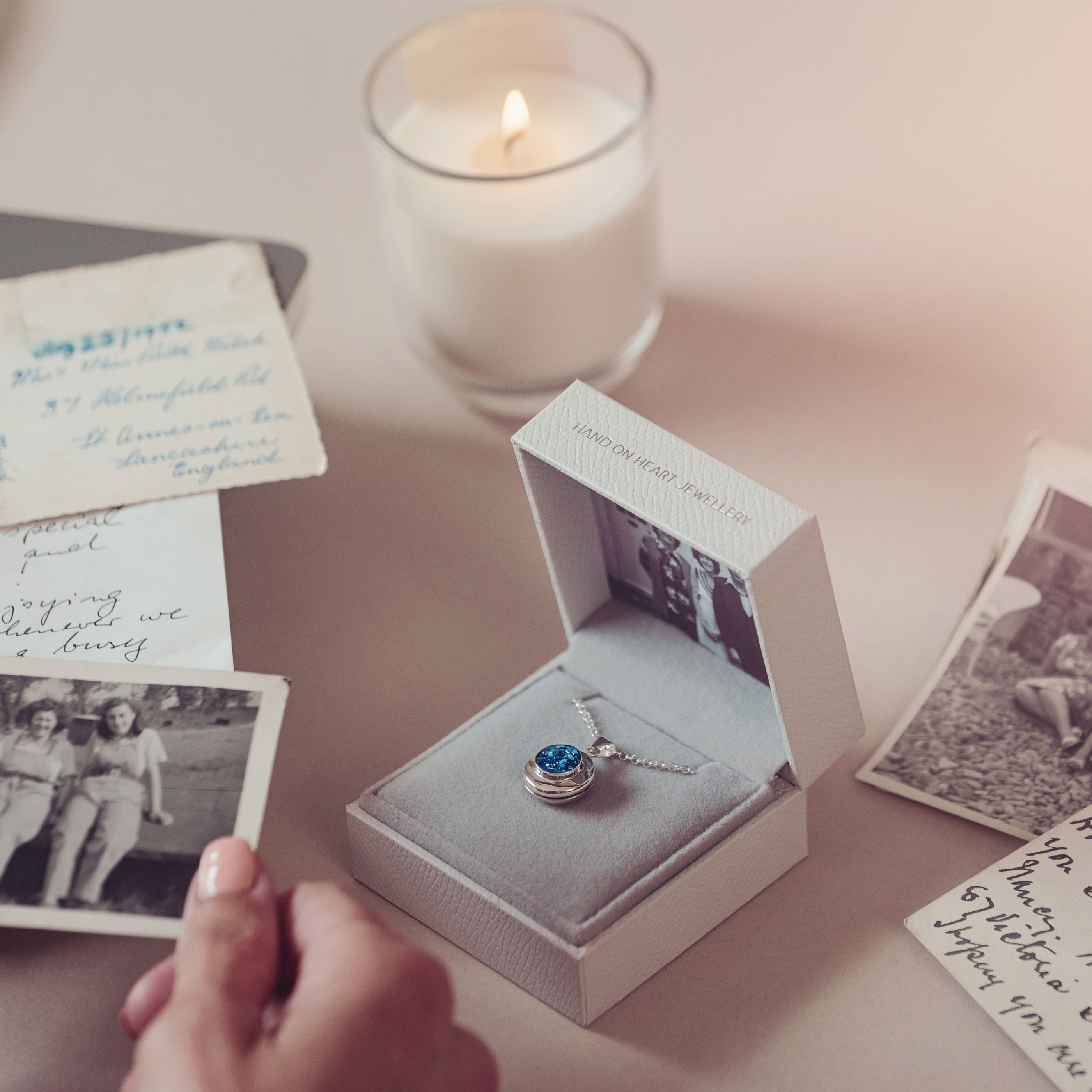 blue cremation ashes locket in a grey jewellery box and a womans hand holding a photograph