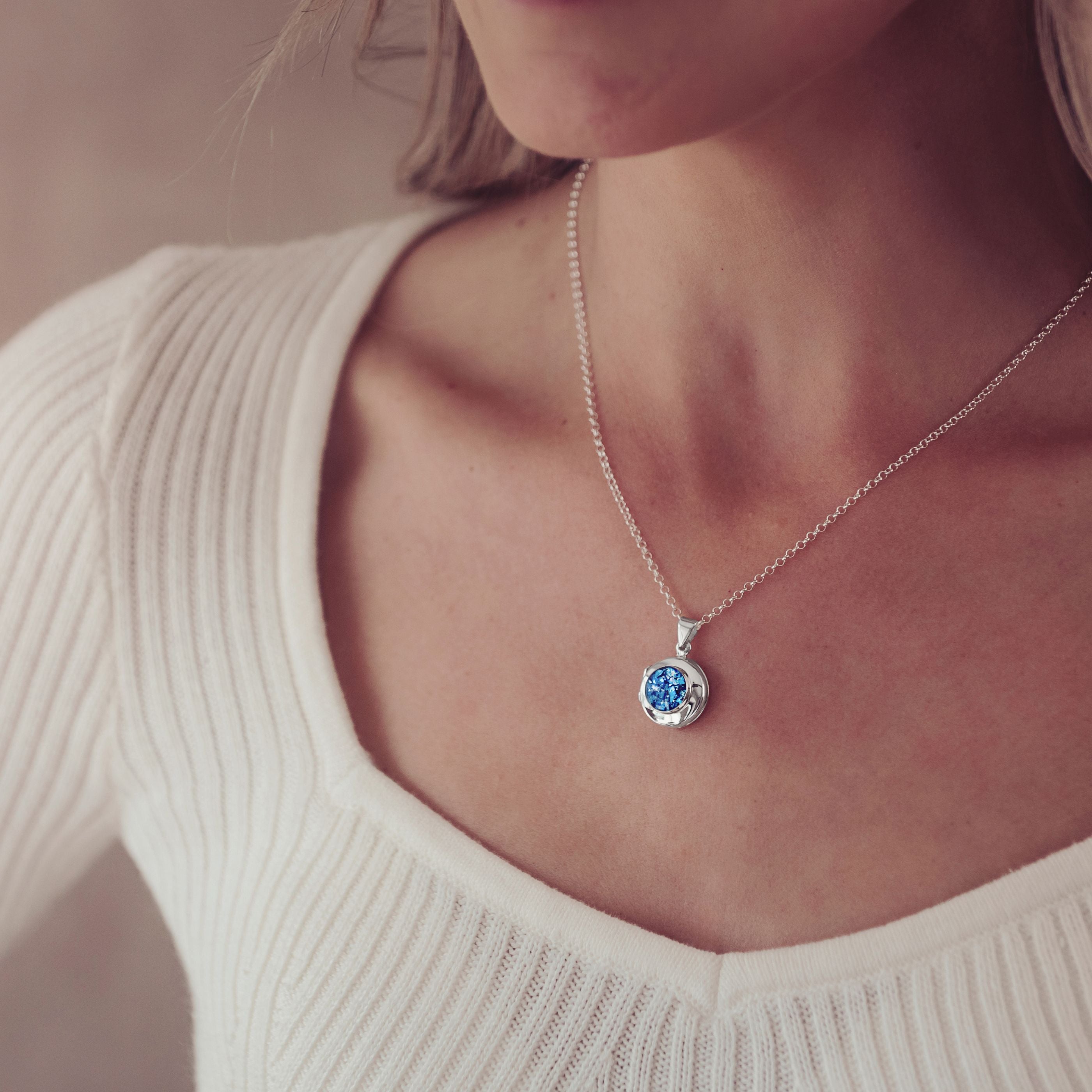 a silver and blue locket necklace filled with cremation ashes worn on a blonde lady's neck