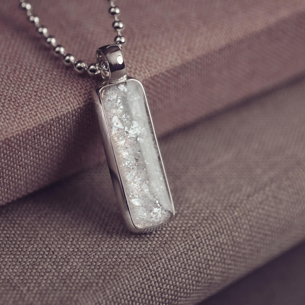 A sophisticated Mens silver necklace featuring a rectangular pendant filled with shimmering white crystal and resin, delicately layered with cremation ashes, showcased against a dark background on a silver ball chain