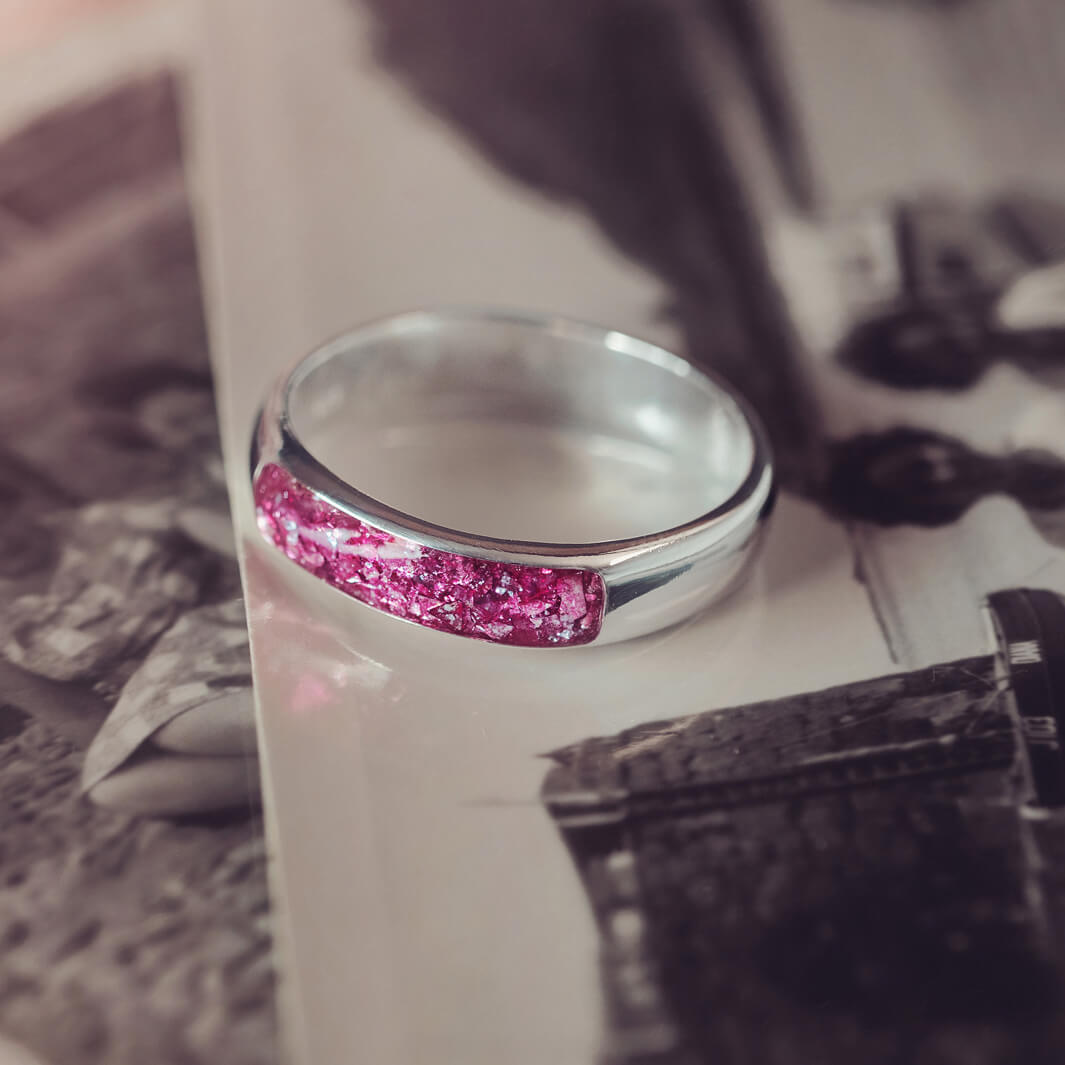 Sterling silver Mens Band Ring with a central section filled with memorial ashes and pink crushed crystals, displayed on top of an old photo