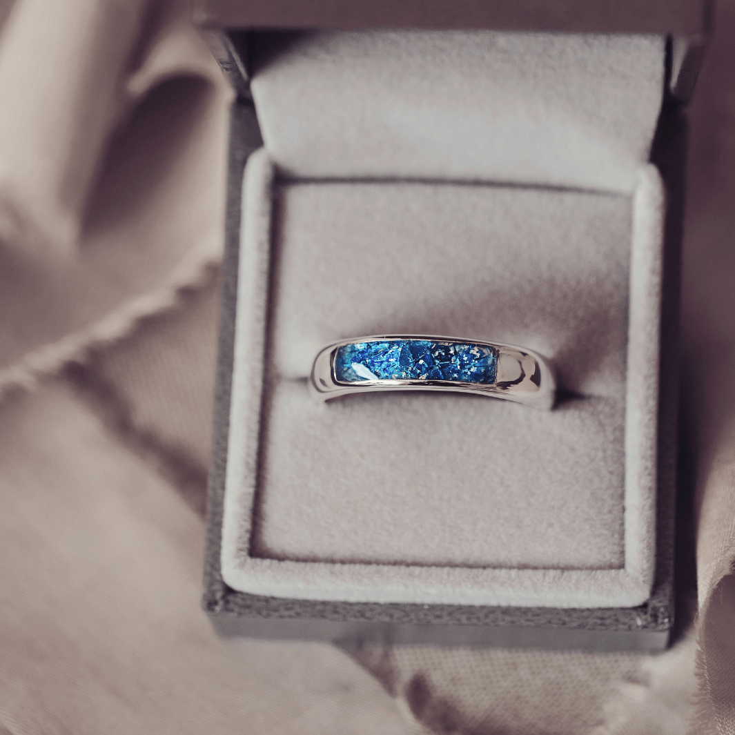 Sterling silver Mens Band Ring with a central section filled with memorial ashes and blue crushed crystals, displayed in a grey jewellery box