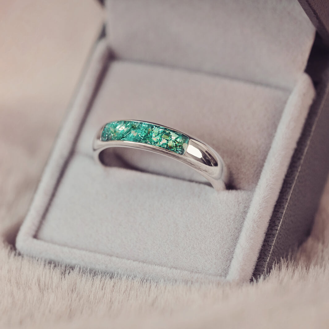 Sterling silver Mens Band Ring with a central section filled with memorial ashes and green crushed crystals, displayed in a grey jewellery box