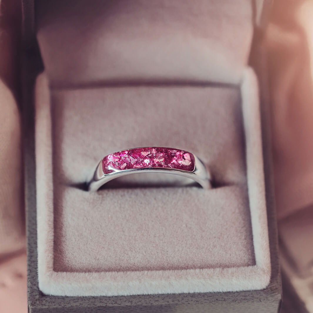 Sterling silver Mens Band Ring with a central section filled with memorial ashes and pink crushed crystals, displayed in a grey jewellery box