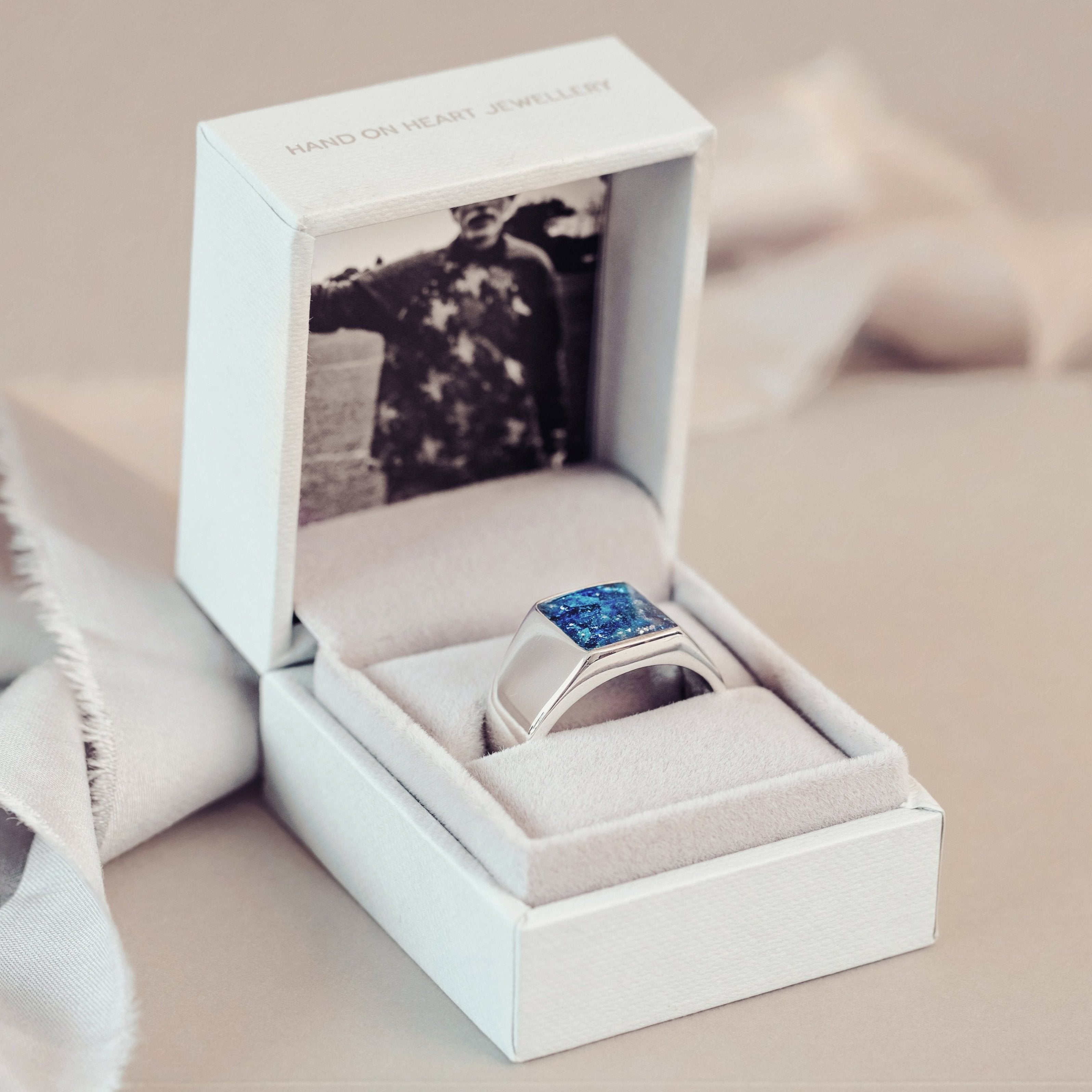 A mens cremation ashes signet ring displayed elegantly in a box adorned with ribbon