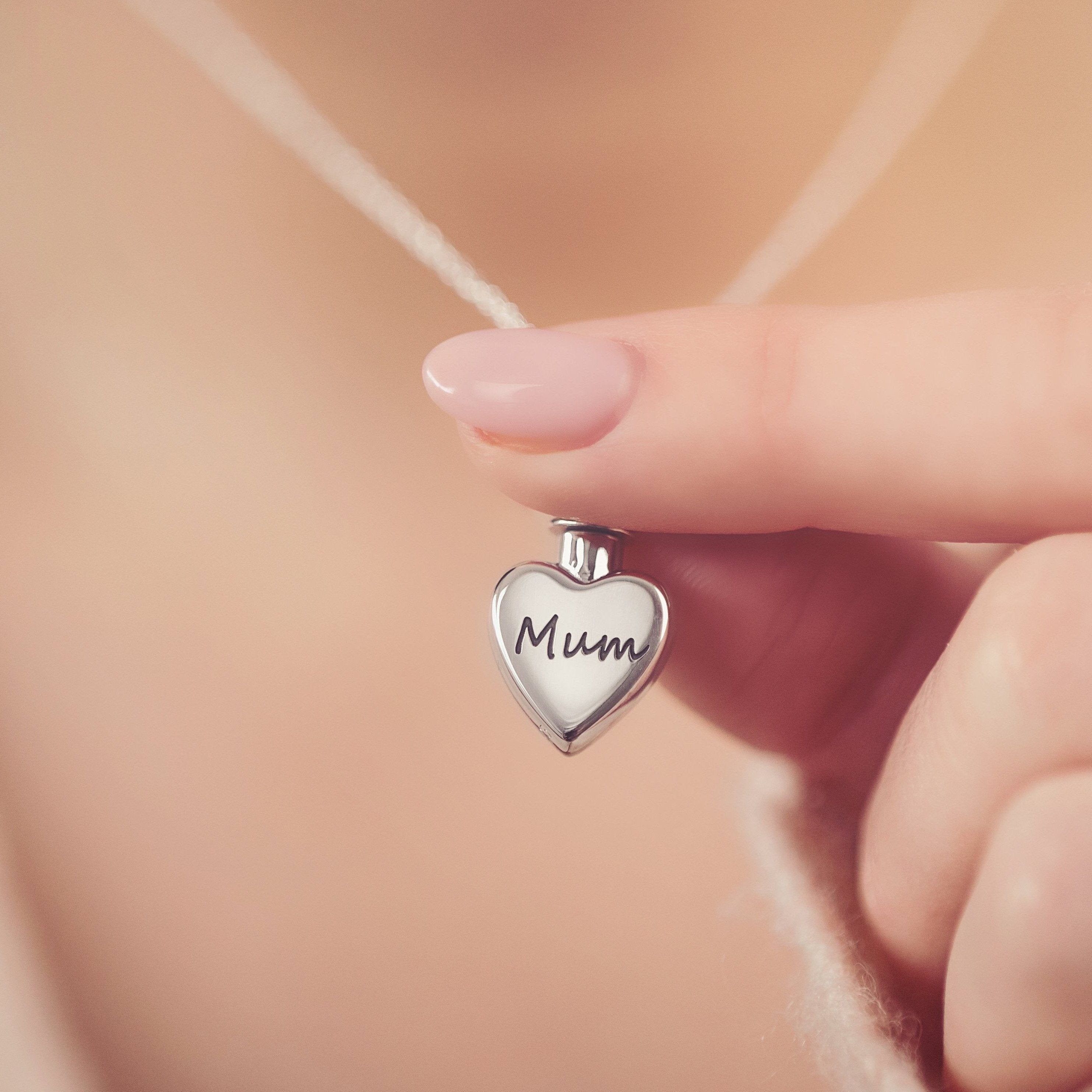 Close-up of a woman holding a silver heart ashes locket, personalised and engraved with 'Mum'