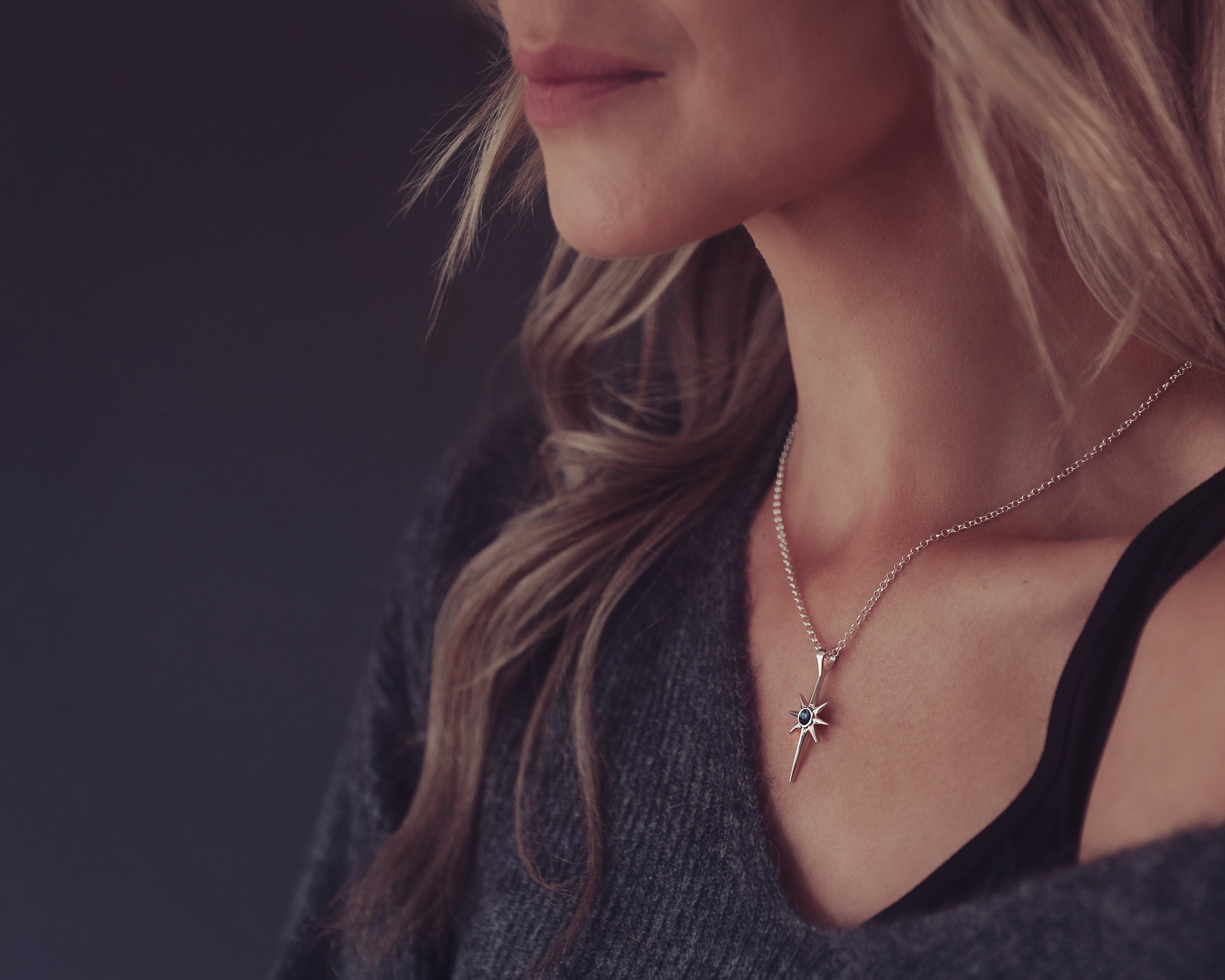 A woman with blonde hair and a grey jumper elegantly wearing a silver north star cremation ashes necklace