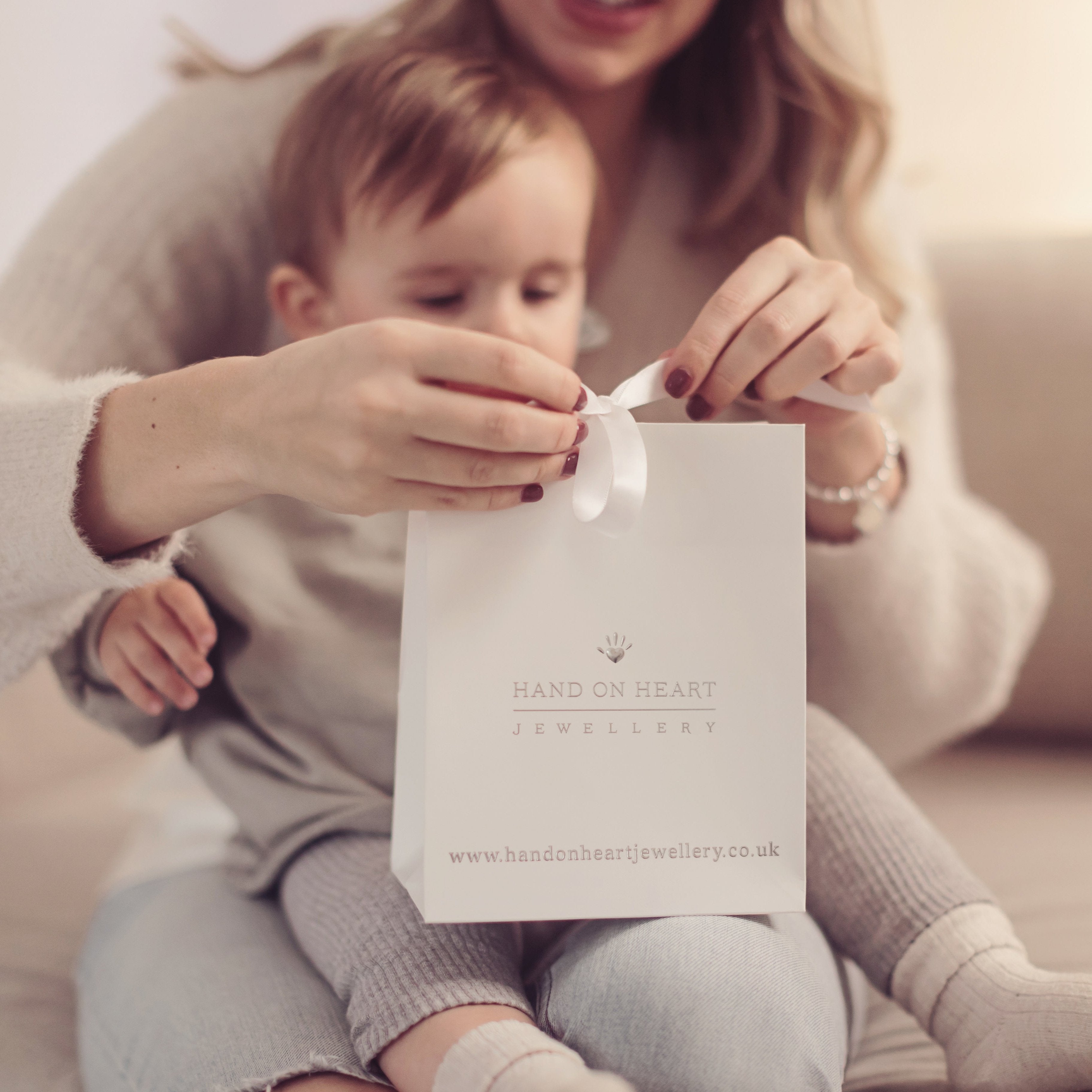 A woman cradles a baby while untying a white gift bag 