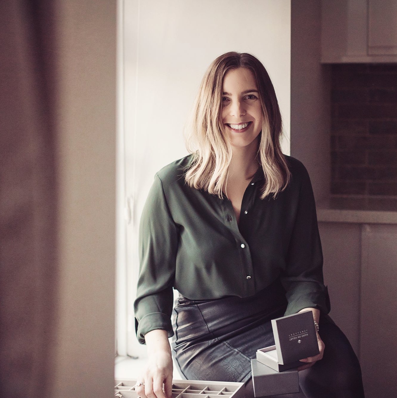 Managing director, Amanda, sitting on a window sill whilst holding a Hand on Heart Jewellery box