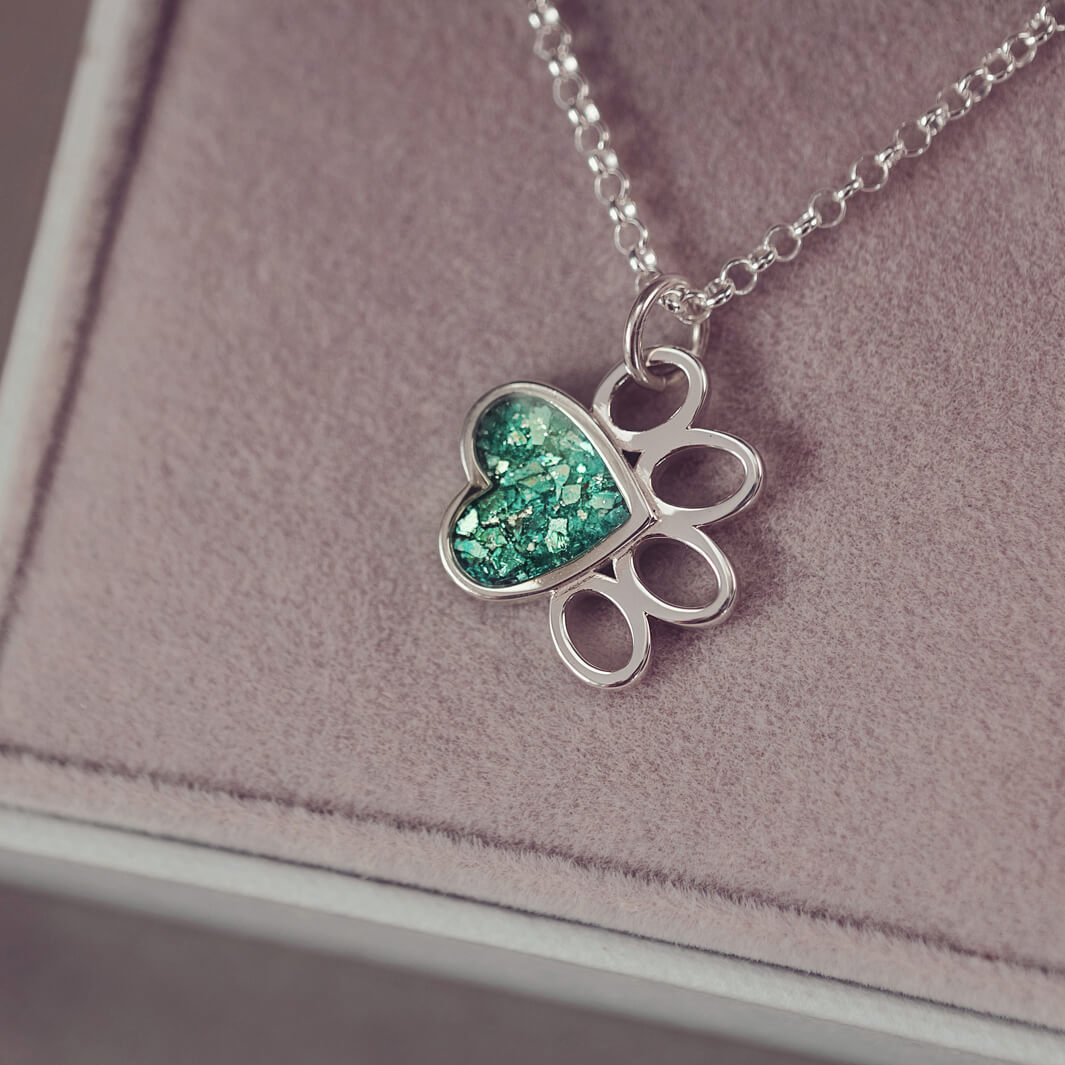 A Pawprint Shaped Sterling Silver Necklace, where the main pad is filled with green crystal and cremation ashes. Hanging from a sterling silver belcher chain in a grey jewellery box.