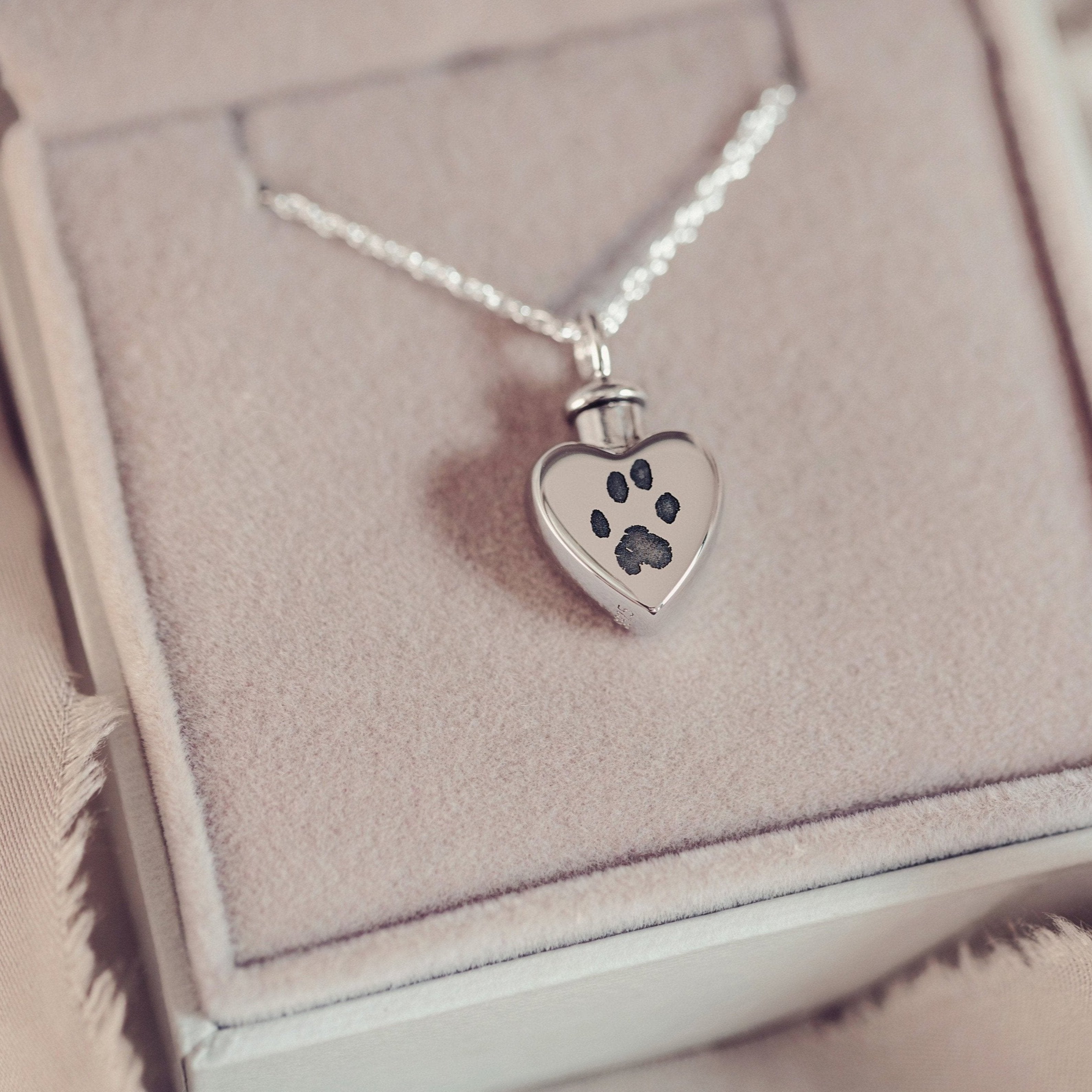 A small heart locket featuring a paw print, designed to hold pet's cremation ashes