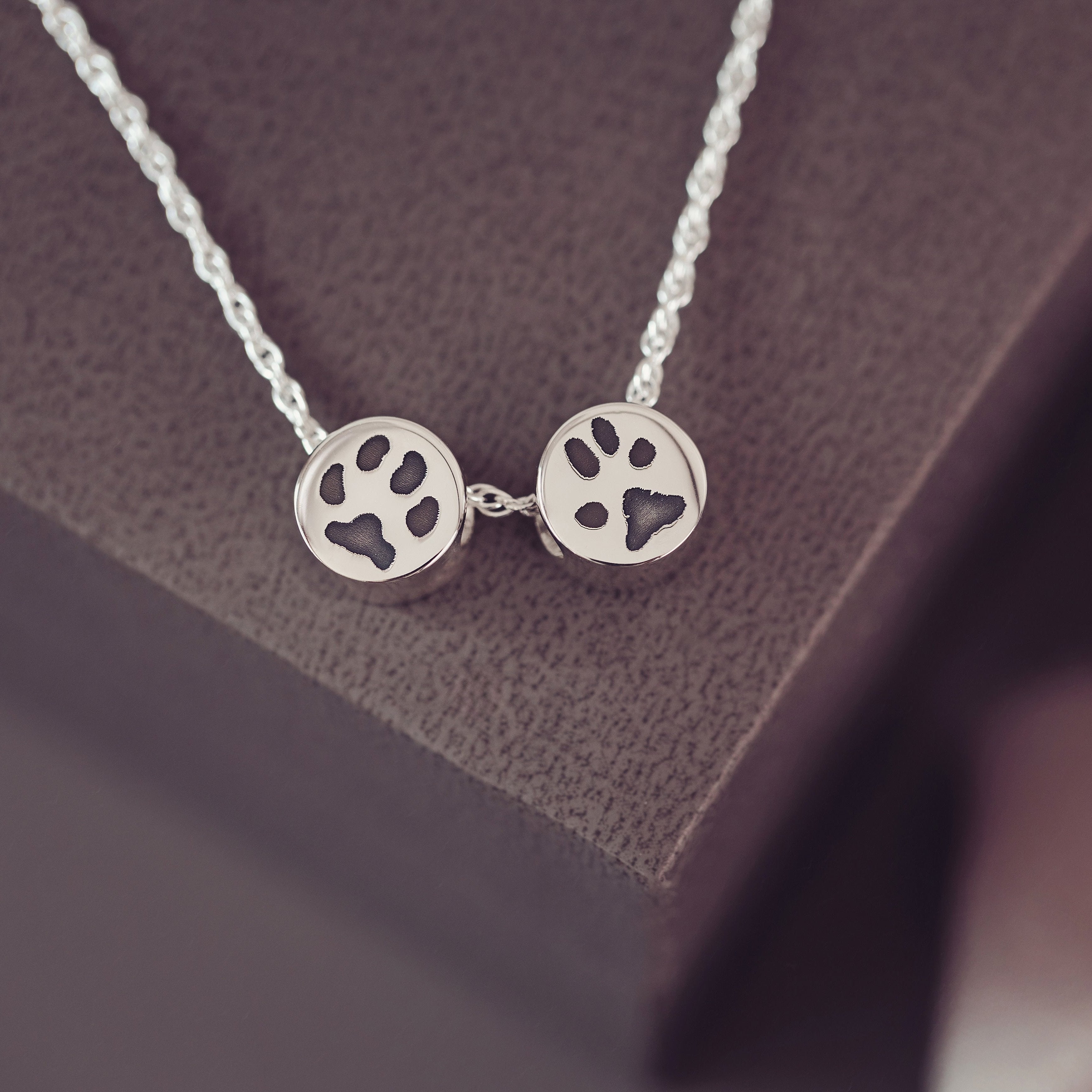 A silver necklace featuring two round charms featuring pawprints