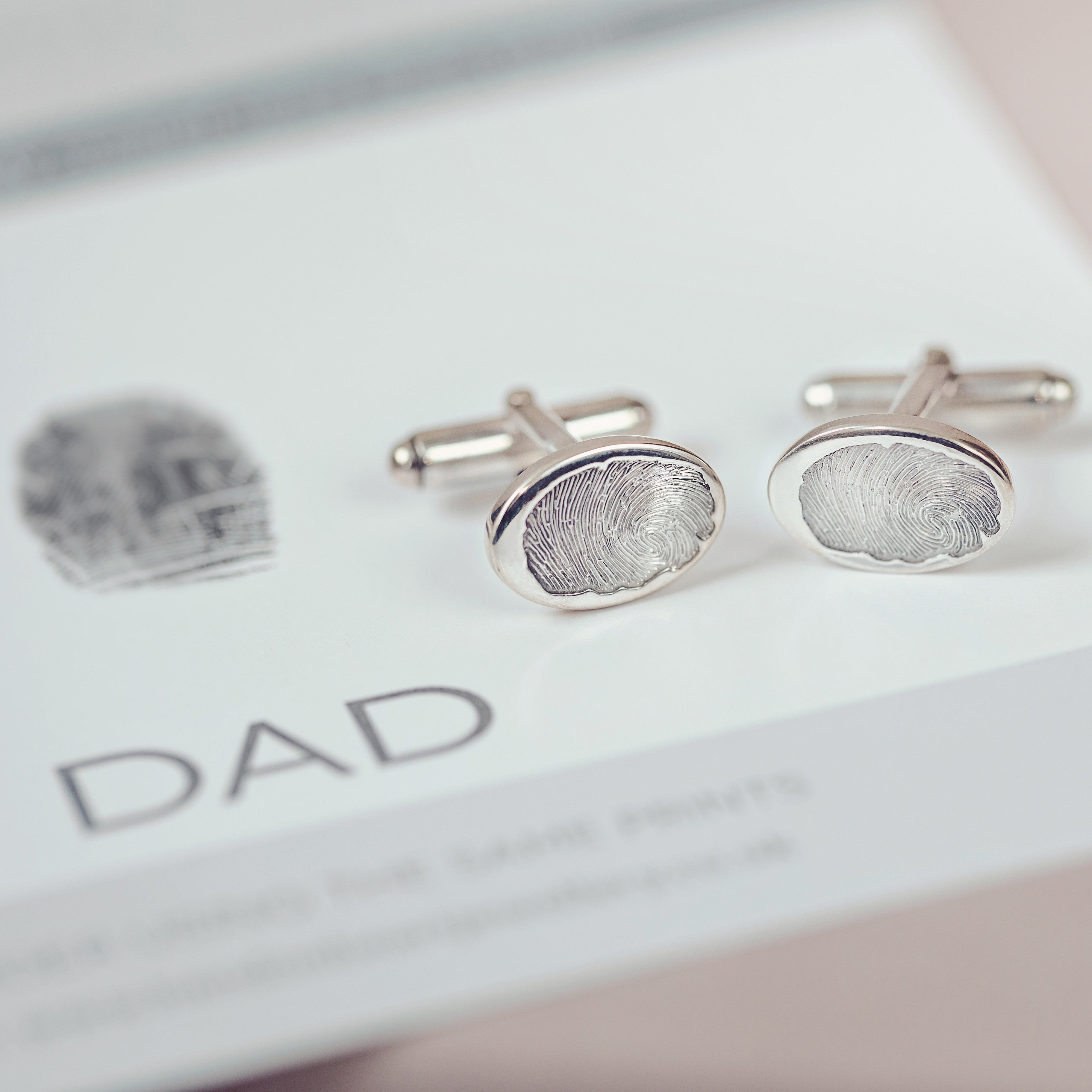 A pair of silver fingerprint cufflinks created using Dad's fingerprint displayed next to them