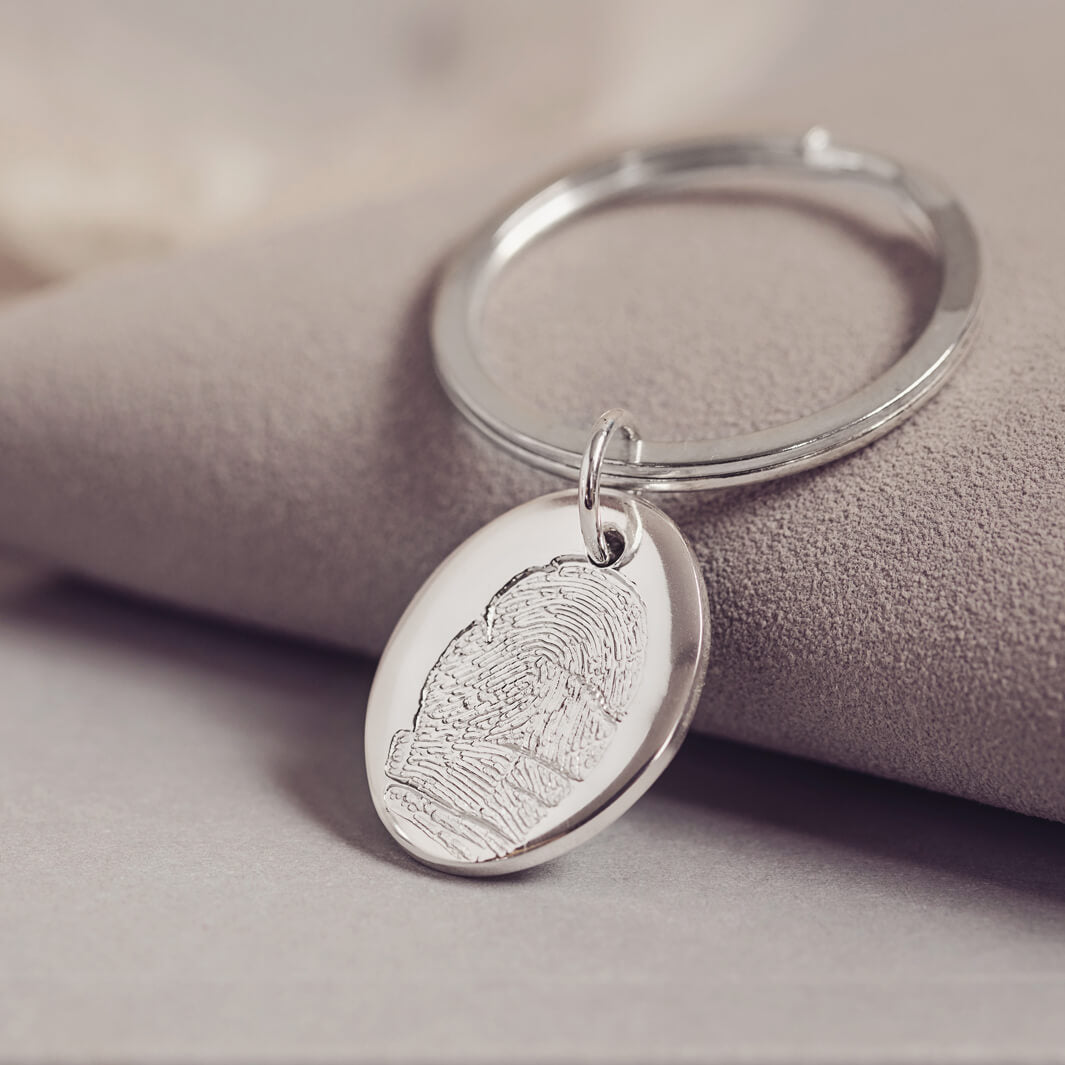 A silver oval keyring featuring a unique fingerprint design resting on a grey surface