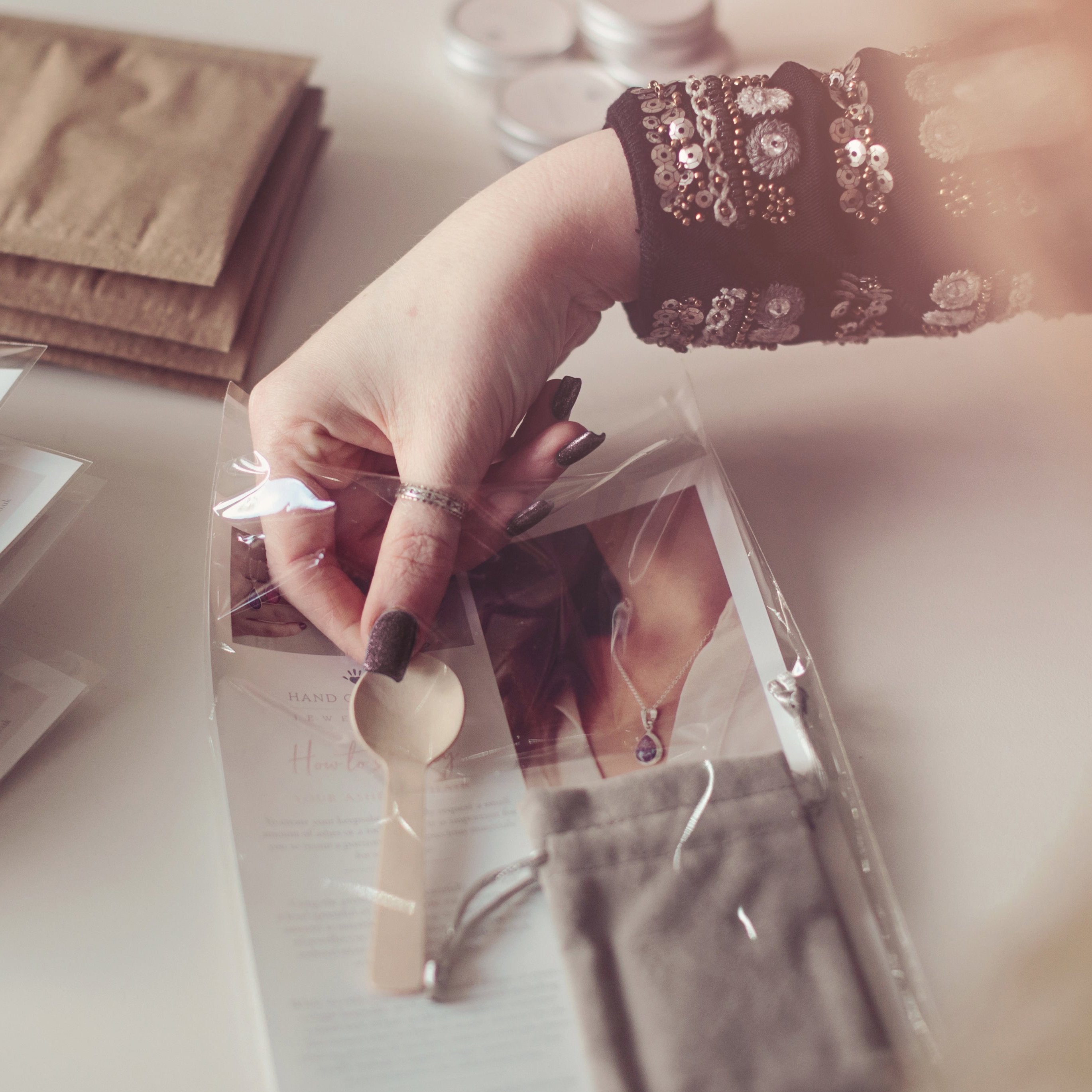 Close up of woman's hand adding spoon into ashes collection pack. In the background, brown envelopes and ashes tins are blurred