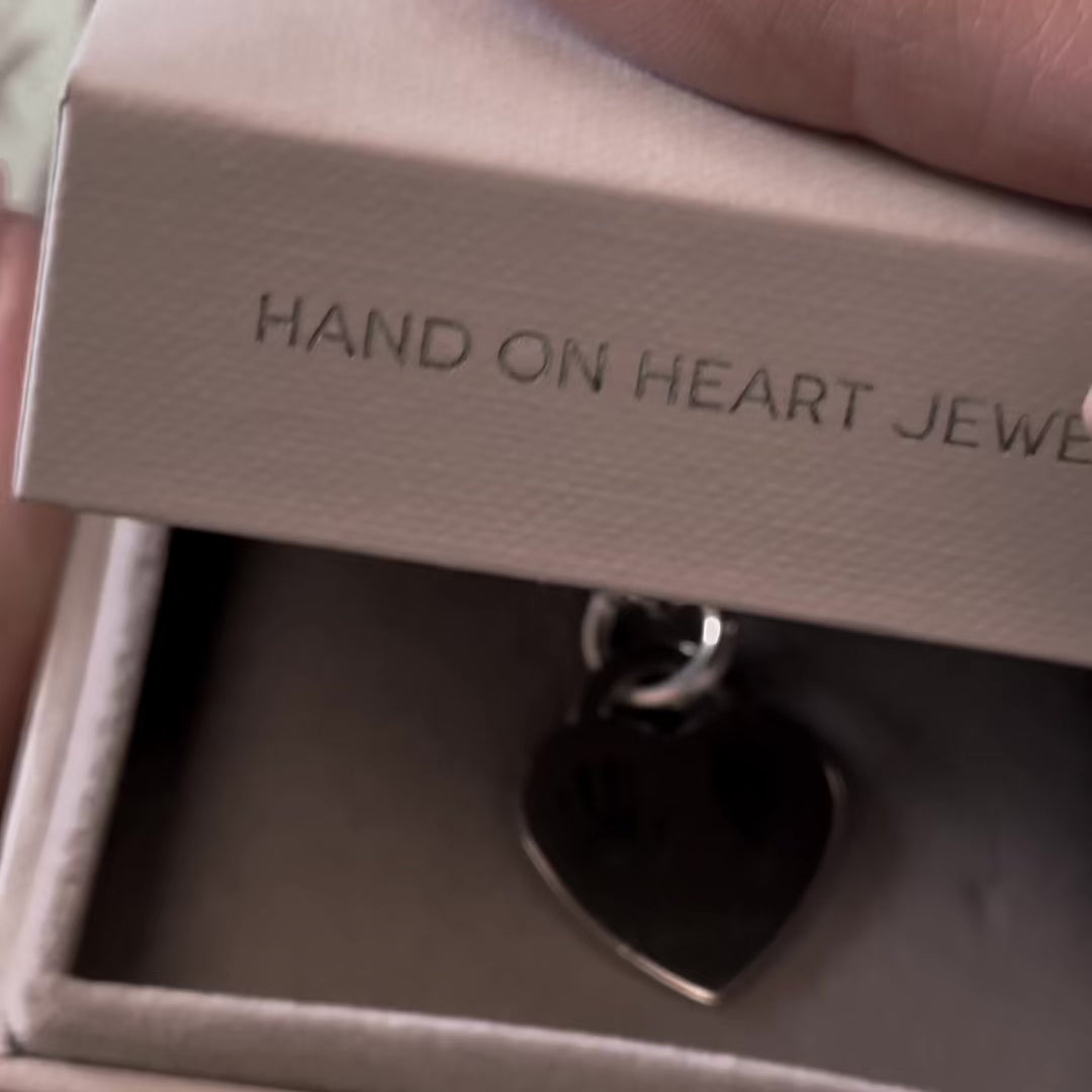 Showing a silver heart necklace with a handprint and footprint engraved and the name