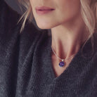 a round purple necklace filled with cremation ashes worn on a lady with blond wavy hair