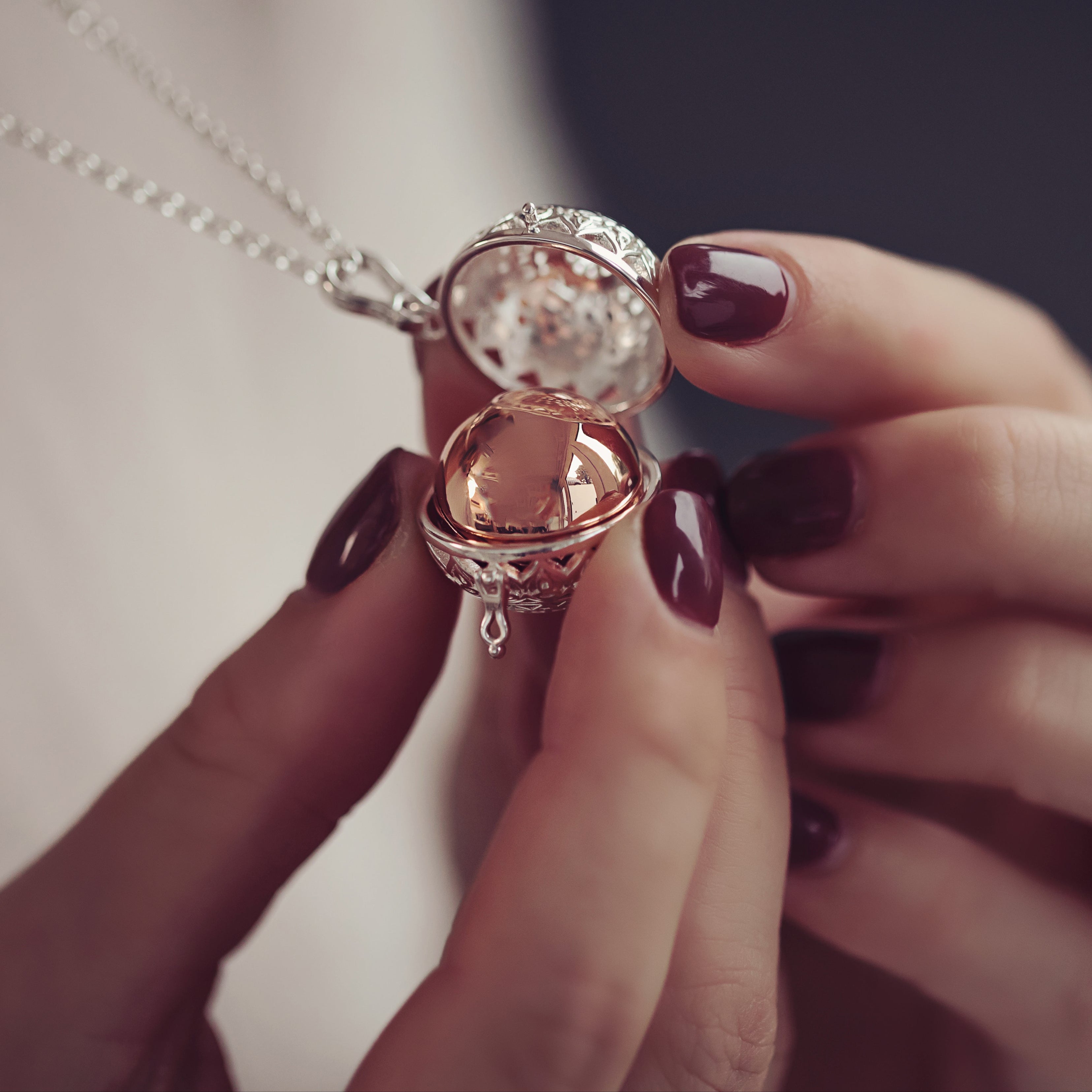 A close up of a woman's hands delicately holding a patterned ashes urn locket necklace