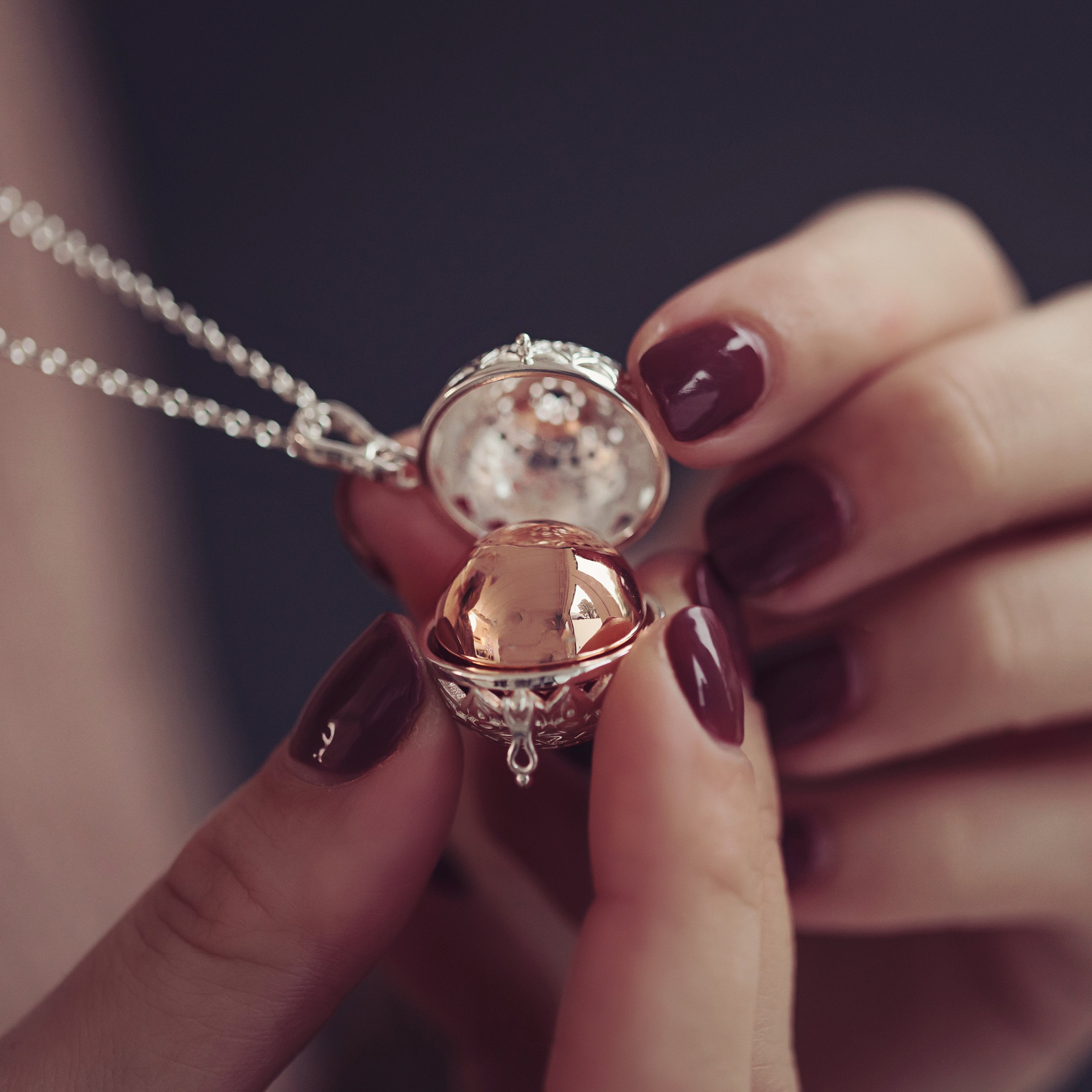 Close-up of a woman's hands opening a self-fill patterned ashes locket, revealing the rose gold sphere inside