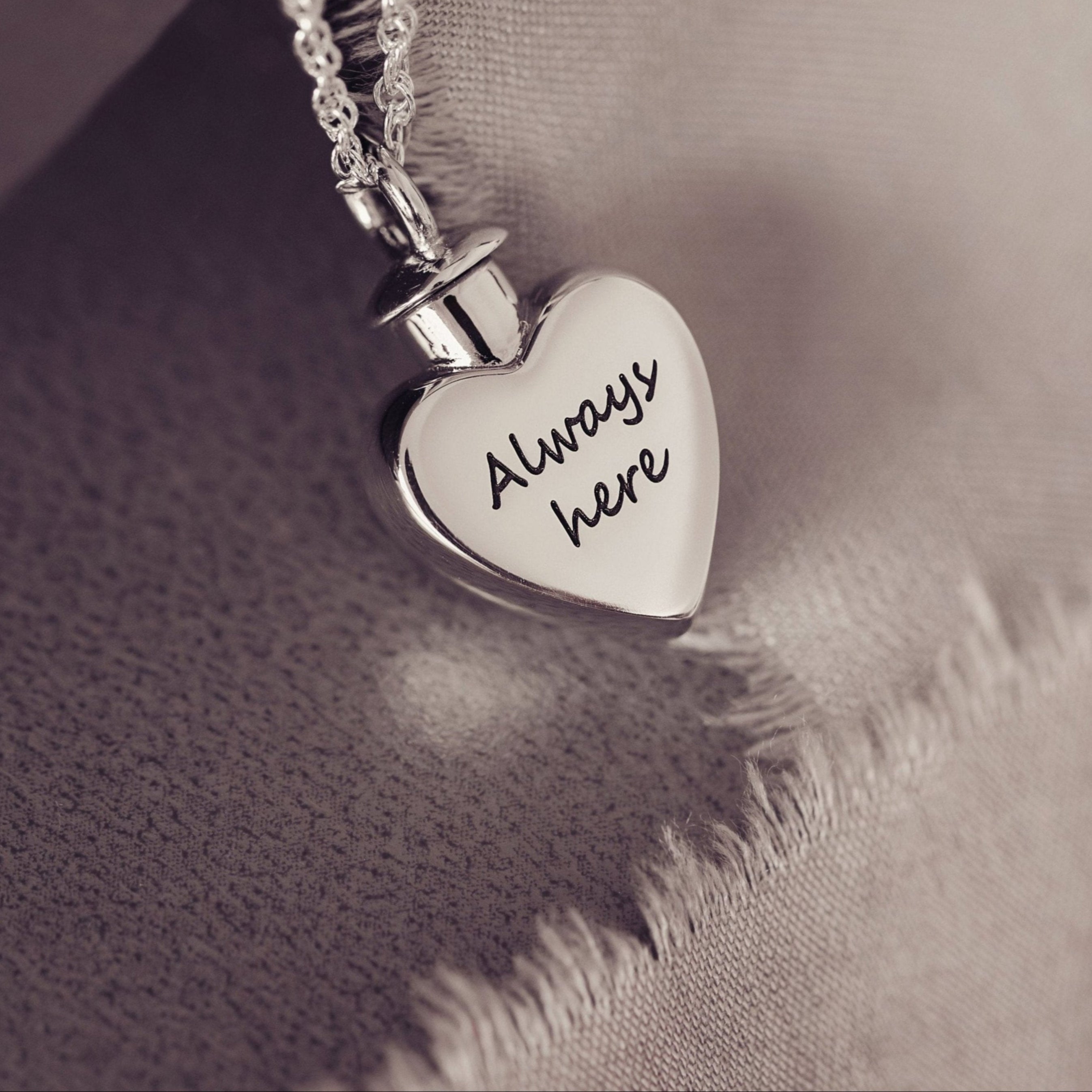 A heart shaped locket designed to hold cremation ashes personalised with message 'Always here'