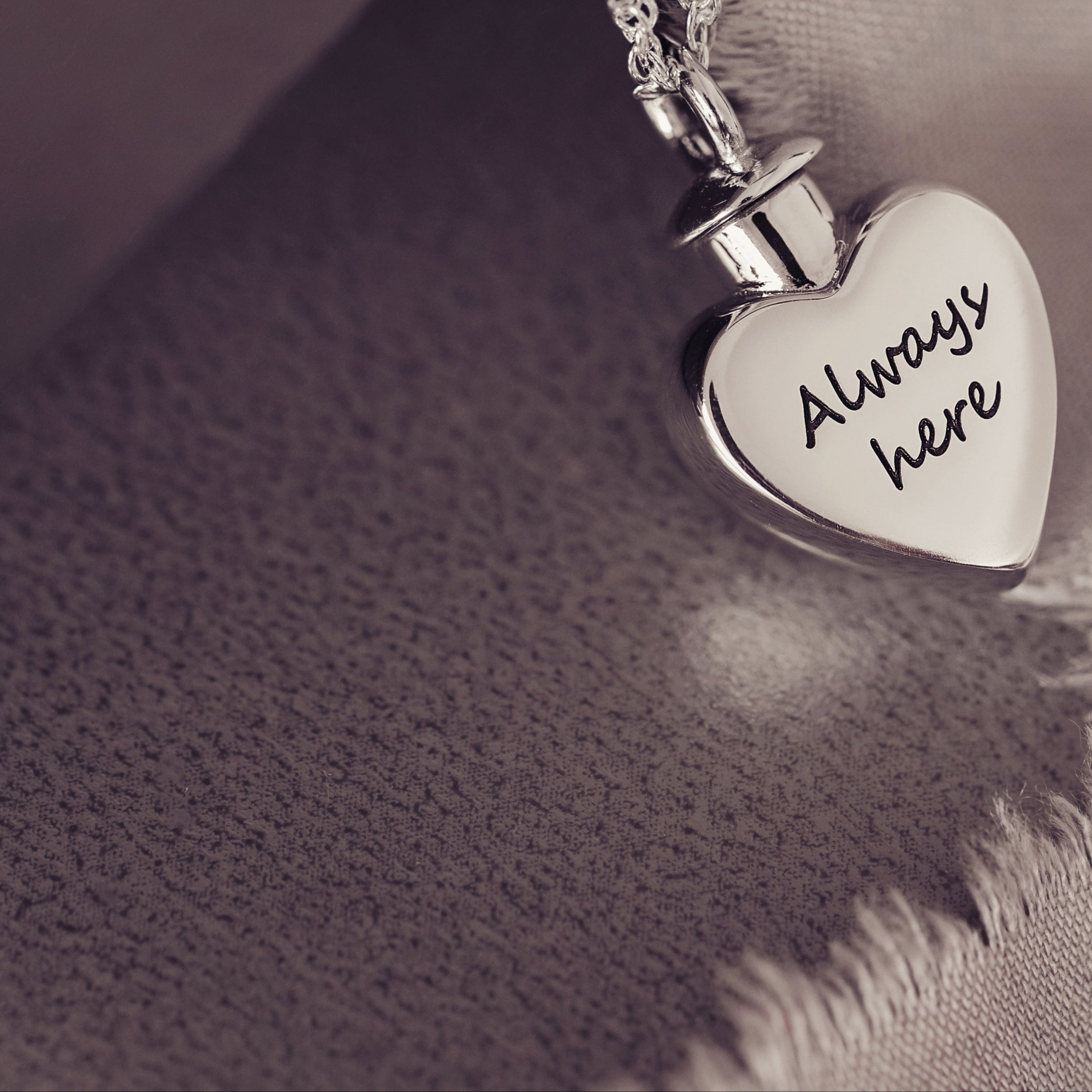 A close up of a silver personalised self fill cremation ashes personalised locket engraved with message 'Always here'