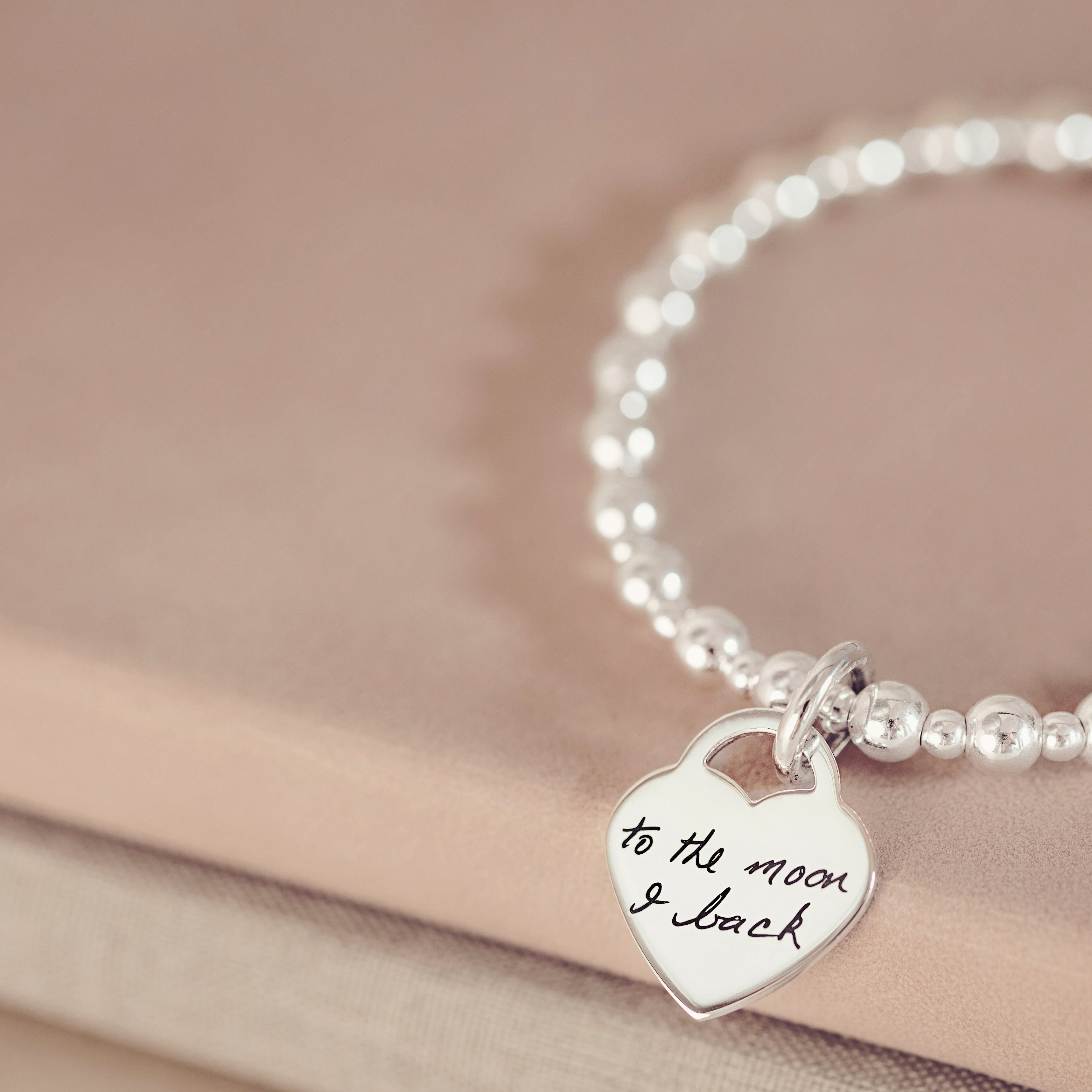 A silver bead bracelet featuring a heart charm with a handwritten message 'to the moon & back'