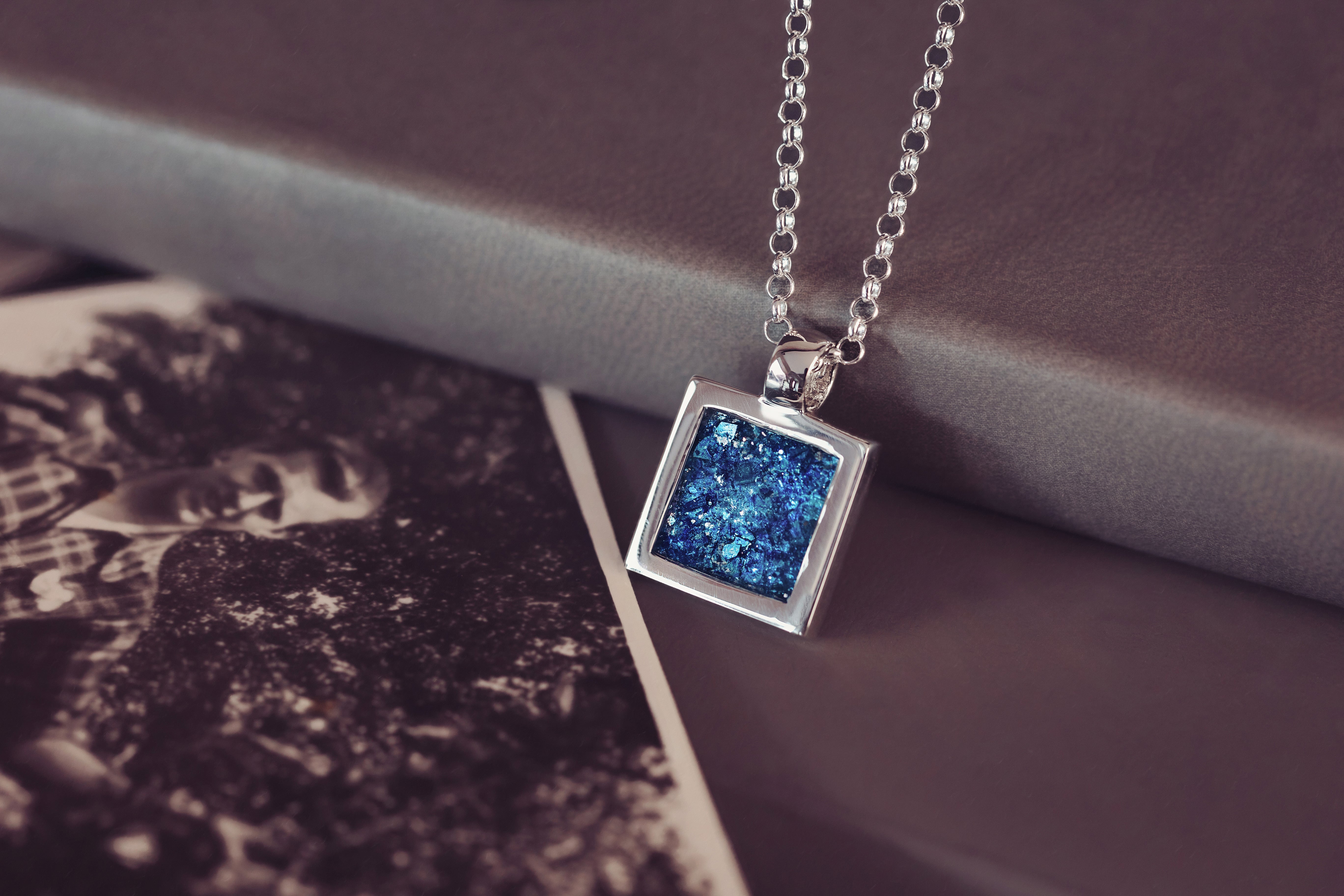 A blue square pendant on a chain, containing cremation ashes