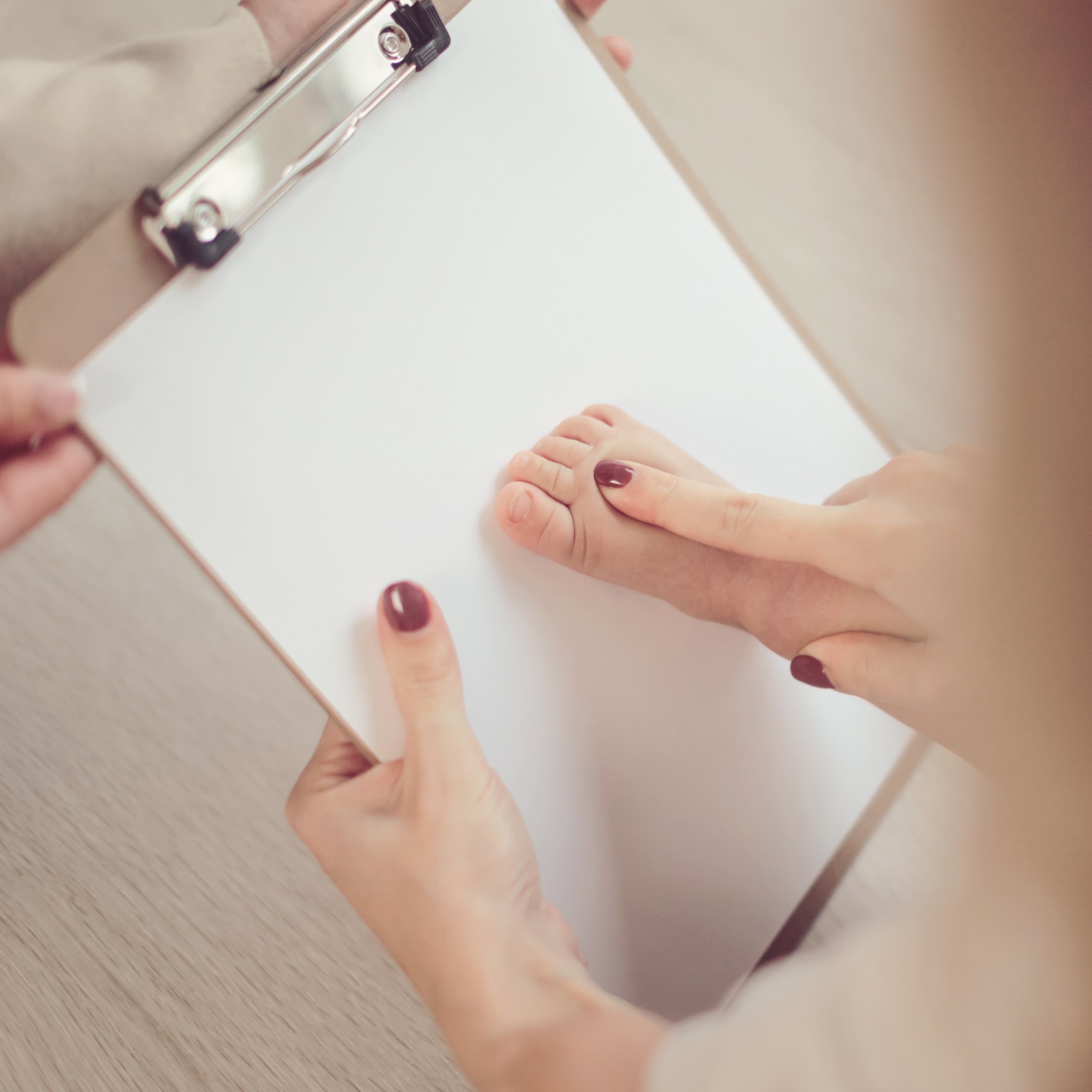 A woman holding a clipboard while using an inkless print kit to take a baby's footprint