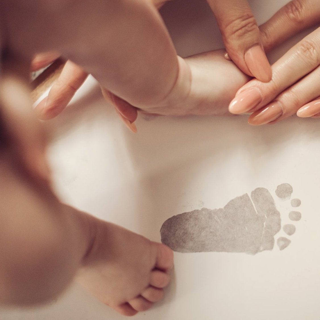 A woman gently holds a baby's foot, capturing baby's footprints using the inkless print kit