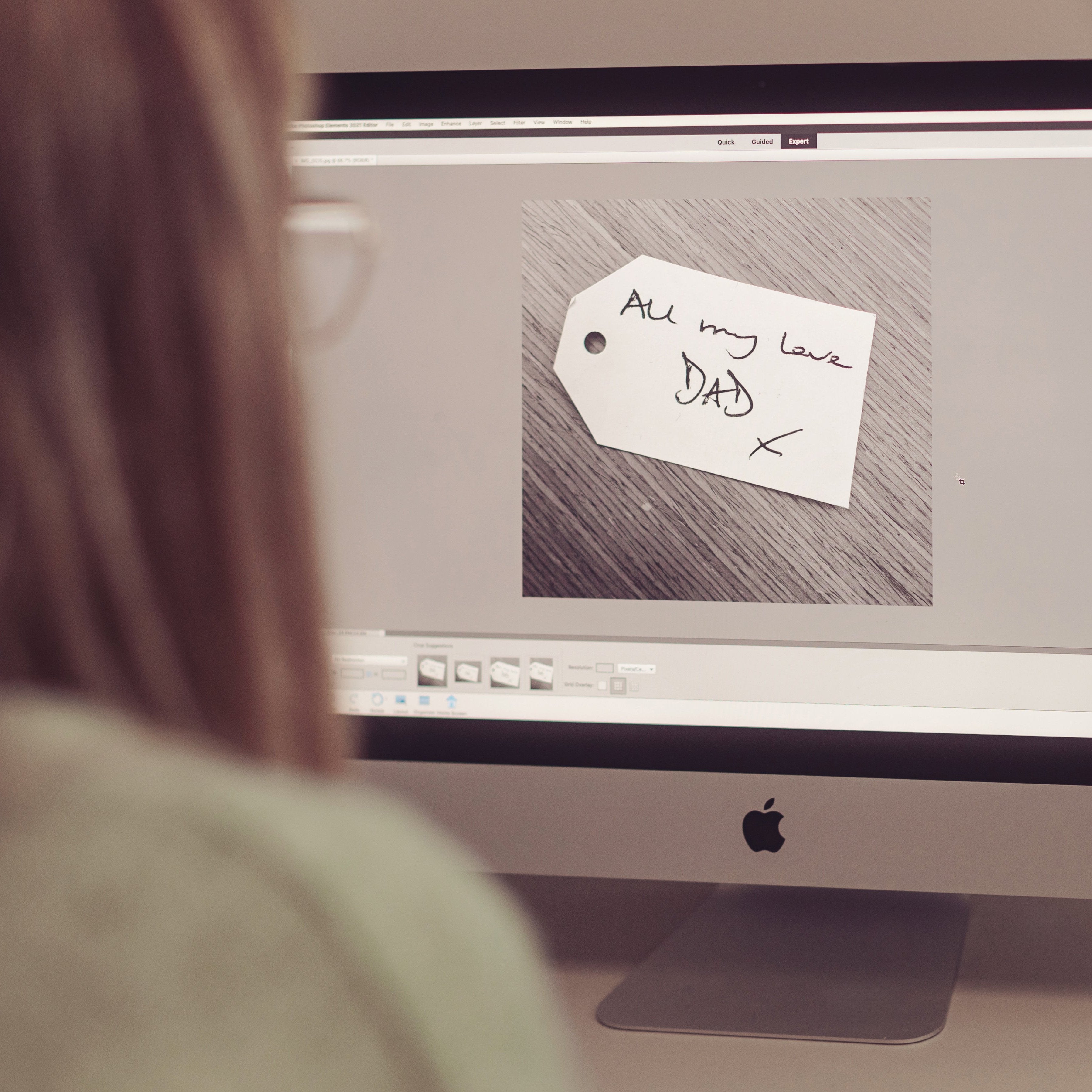 A woman looking at a computer screen displaying a handwritten note with the message 'All my love Dad x'