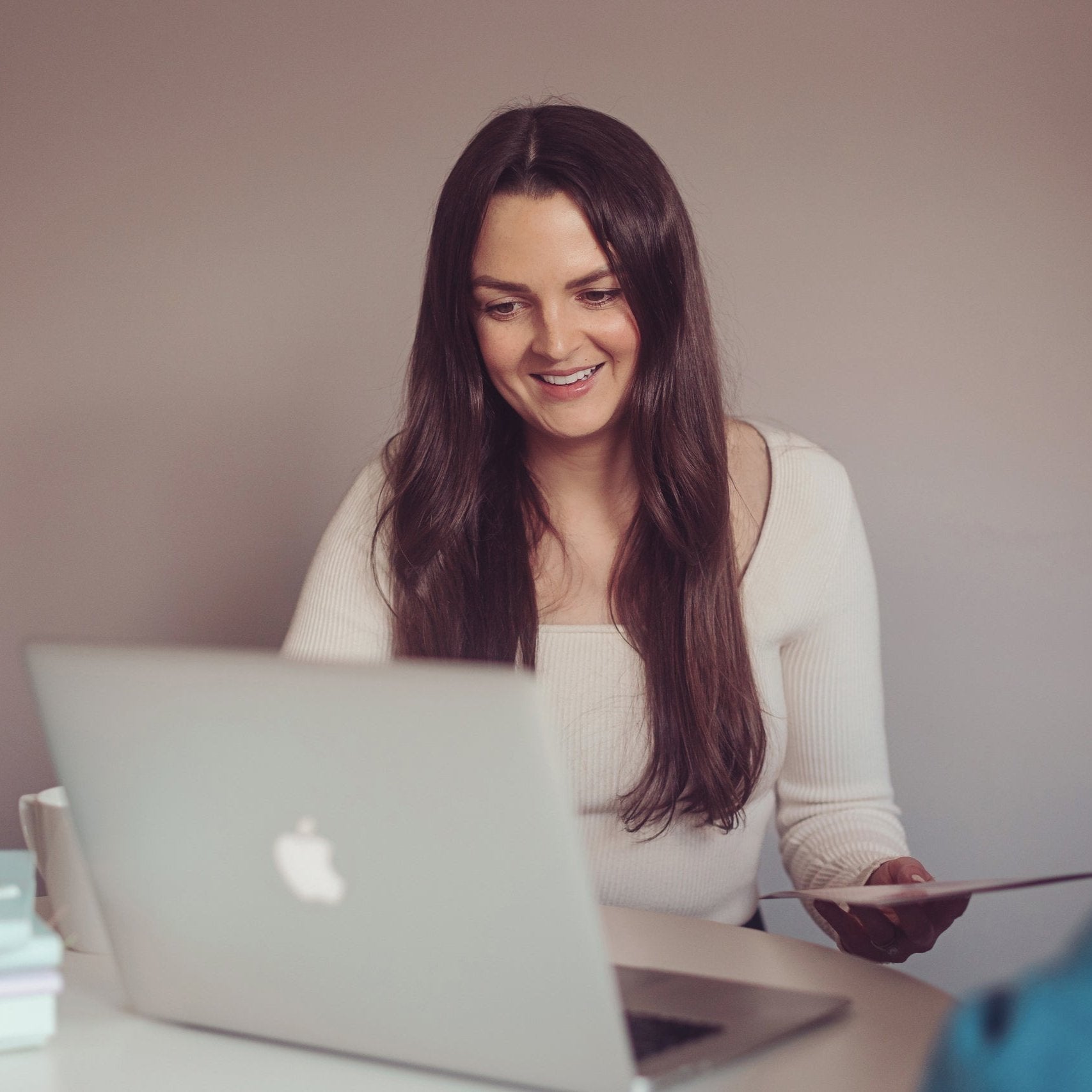 Woman seated at a table working on a laptop with a brochure in one hand