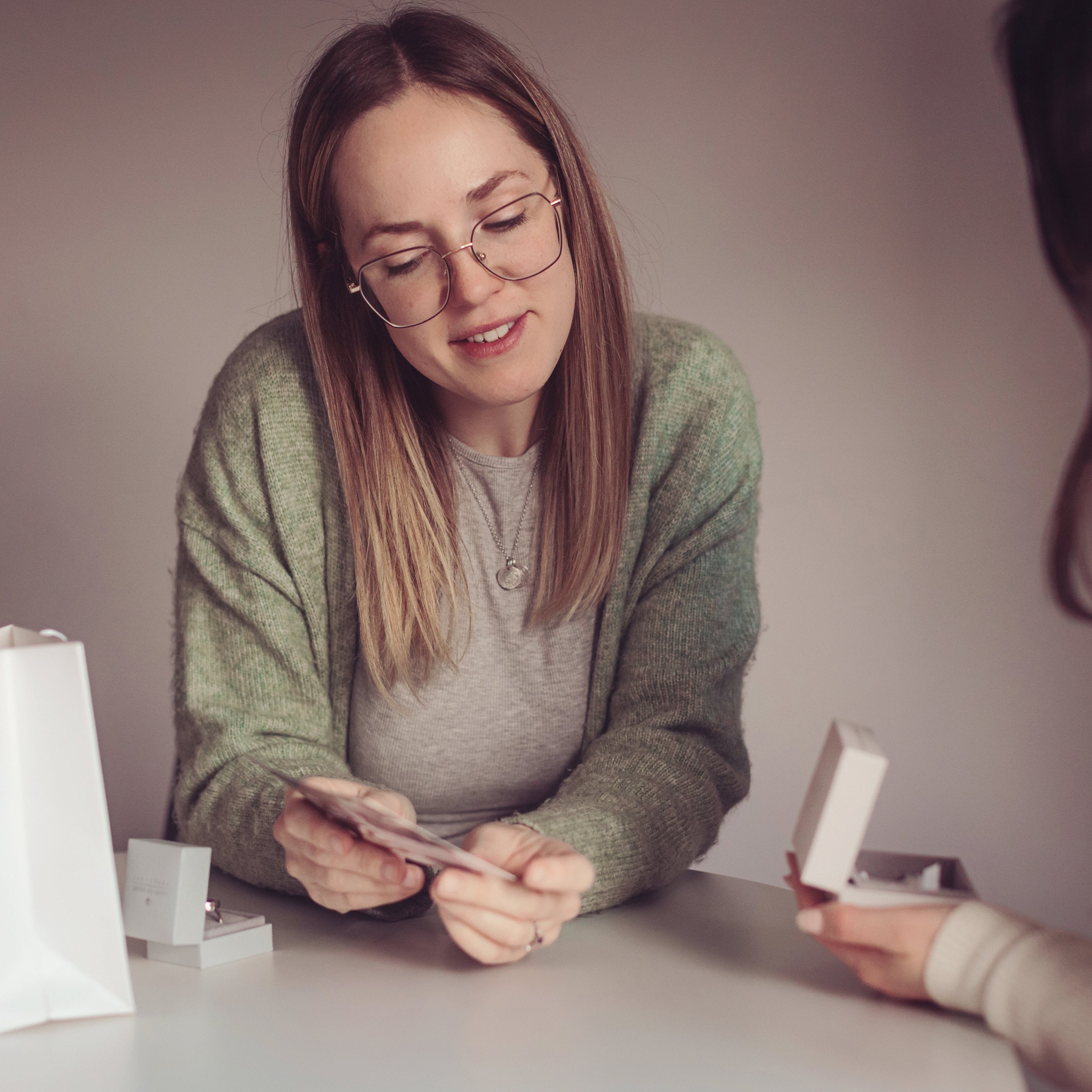 Team member sitting at a table, showing product details to a customer featuring a branded gift bag and jewellery box