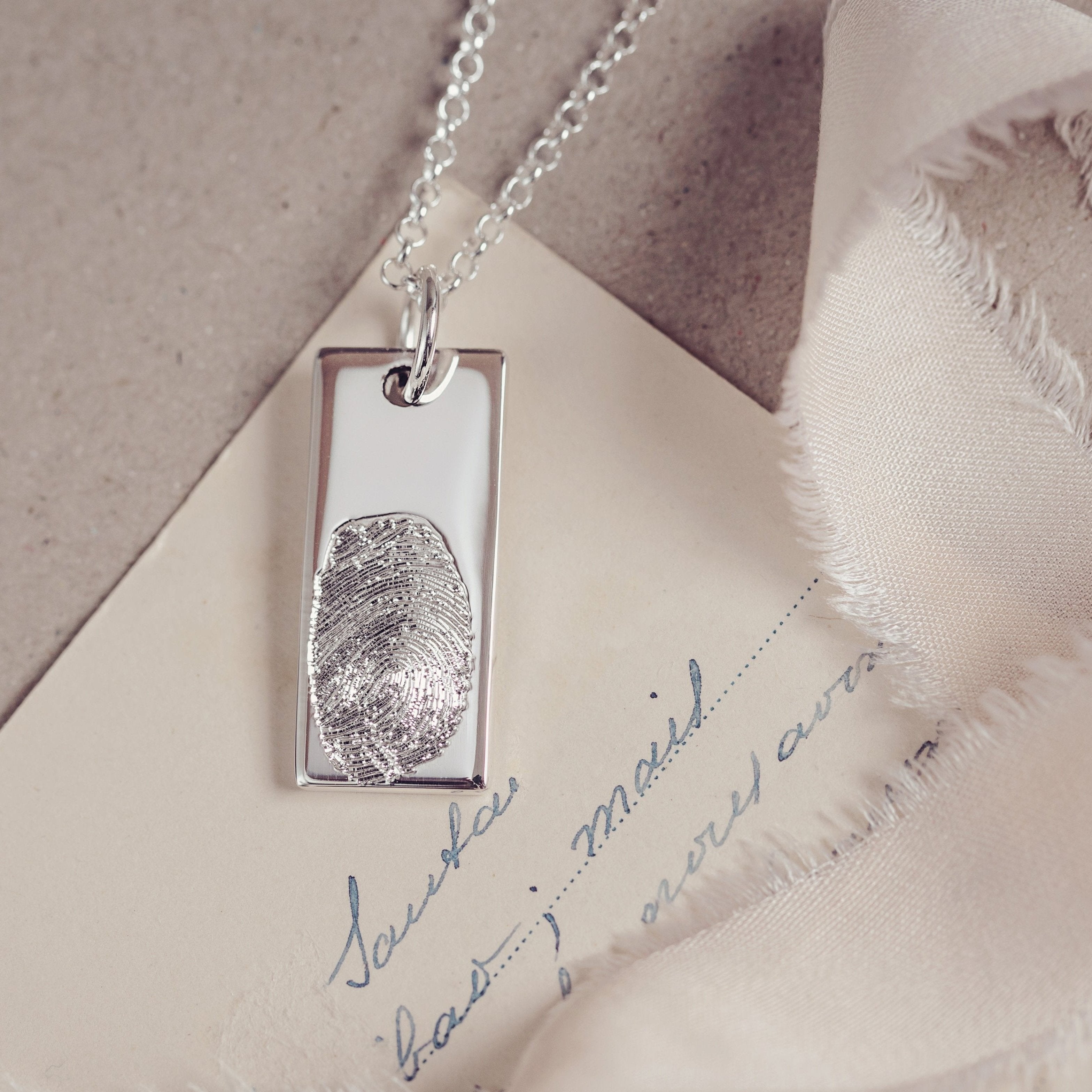 A close up of a fingerprint tag necklace resting on a sheet of paper featuring handwriting in blue ink