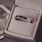 Sterling silver womens ring band with a central section filled with  memorial ashes and black crushed crystals, displayed in a grey jewellery box