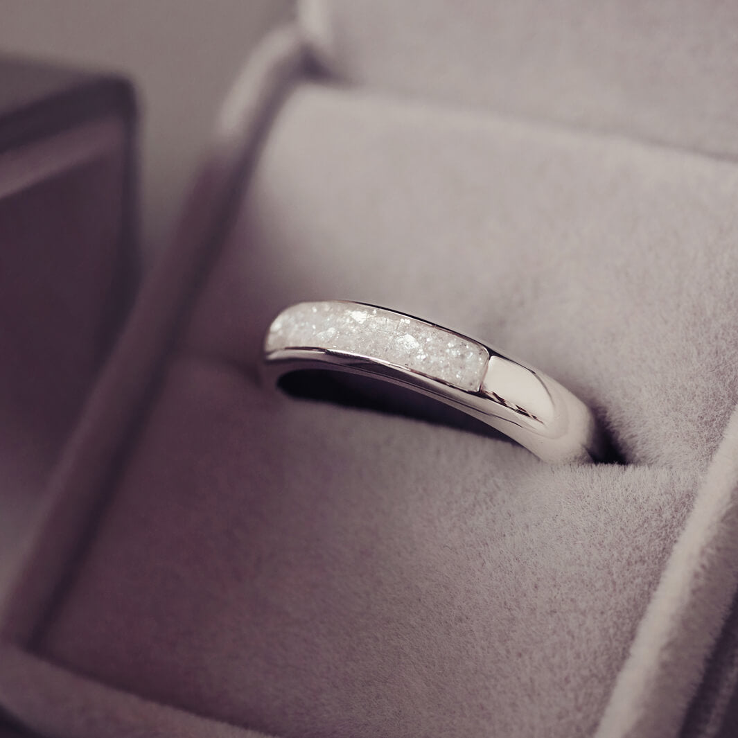 Sterling silver womens ring band with a central section filled with  memorial ashes and clear crushed crystals, displayed in a grey jewellery box