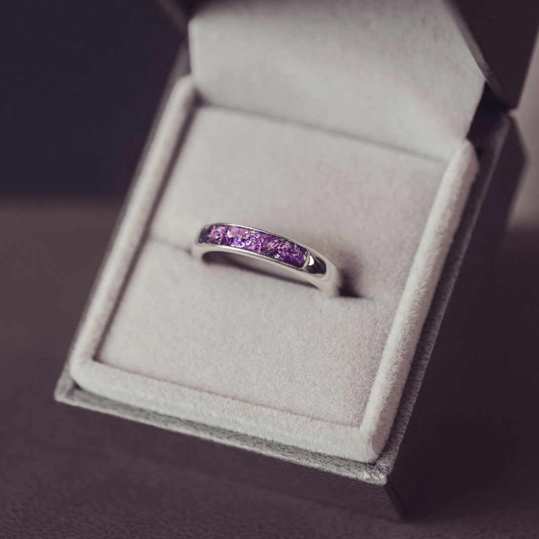 Sterling silver womens ring band with a central section filled with  memorial ashes and purple crushed crystals, displayed in a grey jewellery box