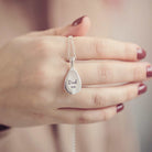 The reverse of a sterling silver teardrop shaped necklace, being held by a ladies hand with red painted nails. There is a message engraved into the back of the pendant which reads 'Dad xx'