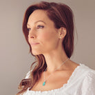 side profile of a brunette last in a white lace top wearing a Sterling silver oval necklace with a central section filled with memorial ashes and green crushed crystals