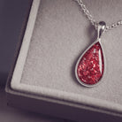 Sterling silver teardrop necklace with a central section filled with memorial ashes and red crushed crystals, displayed in a grey jewellery box